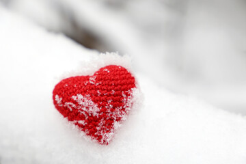 Snow covered red knitted heart in a winter park. Background for Christmas holiday, Valentine's card