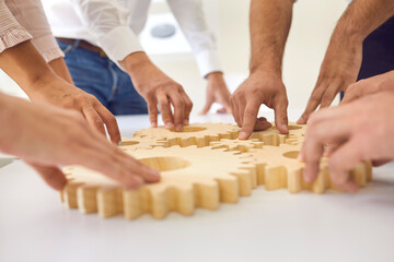 Hands of business people making whole picture of wooden gears on table together