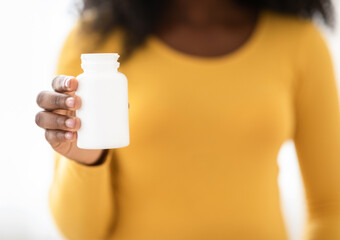 Closeup of black pregnant woman holding white jar with medication