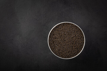 Bowl of black caviar of sturgeon fish on a dark blue background.View from above