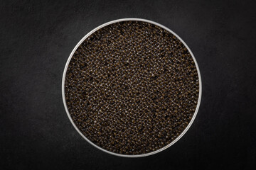 Bowl of black caviar of sturgeon fish on a dark blue background.View from above