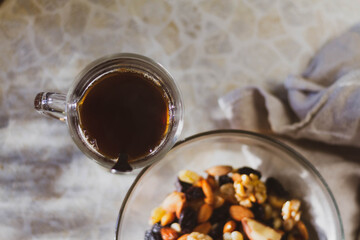 A glass of black coffee on the table, nuts and raisins on a plate.