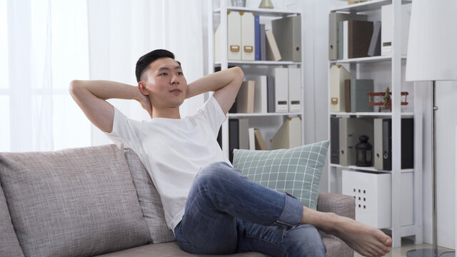 Handsome Asian Chinese Man Relaxing Putting Hands Behind Head And Crossing Legs Feeling Bored At Home Alone.