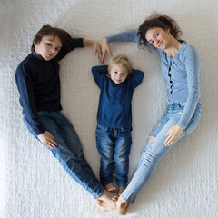 Beautiful family picture of mother and two children, making heart shape, lying on the bed