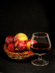 A glass of red wine and apples in a basket on a black background.