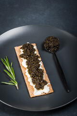 Black caviar of sturgeon in the biscuits with cream cheese. Spoon with caviar. Round blue plate....