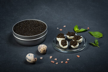 Black caviar of sturgeon in the quail eggs on a dark background. New Year's feast.