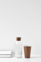 Transparent bottle with cork stopper paper cup and books on a white background. Natural and eco-friendly materials in interior decor. Copy space, mock up