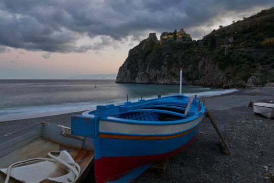A typical wooden fishing boat at the beach under the illuminated Rocca, near Taormina in long exposure.