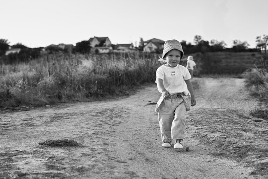 Two-year-old child in a hat walks along a country road, summer. Knowledge of the world. Black and white photo