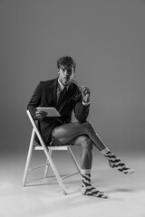 Fototapeta premium Devices. Young fashionable, stylish man wearing jacket and socks working from home. Fashion during insulation 'cause of coronavirus pandemic. Half business and half home style. Black and white.