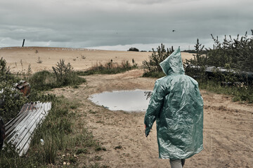 Fototapeta premium A man walks on the sand in the rain in a green raincoat. Lifestyle