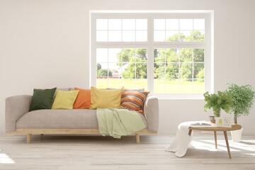 Fototapeta premium White living room with sofa and summer landscape in window. Scandinavian interior design. 3D illustration