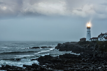 Fototapeta na wymiar Gloomy gloomy photo of a luminous lighthouse on a rocky shore. Famous lighthouse. Portland. USA. Maine