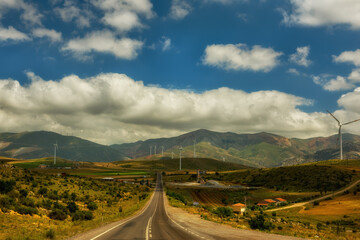 A road among fields and mountainous hills with wind turbines. beautiful hilly landscape.
