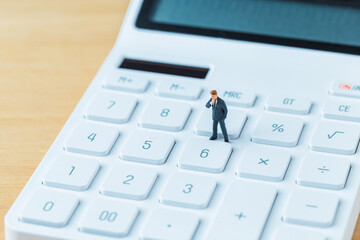 A miniature businessman figure wearing a suit while standing on top of a white calculator