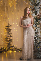 Elegant woman in evening beige fashion dress in golden christmas decorations. Bokeh lights and snowy new year decorated arch. Magic miracle surround full length portrait