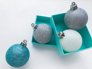 Close-up of shiny Christmas balls blue turquoise, white and silver color with ribbon and blue gift box on a white background. The concept of Christmas and holiday eve