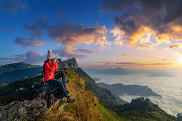 Traveller sitting on the rock and holding camera take photo at Doi pha mon mountains in Chiang rai, Thailand. - obrazy, fototapety, plakaty