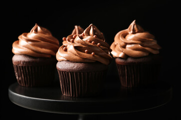 Delicious chocolate cupcakes with cream and beads on black stand, closeup