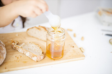 Little girl picking honey from a jar next to a slice of bread