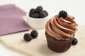 Delicious chocolate cupcake with cream and blackberries on white board, closeup. Space for text