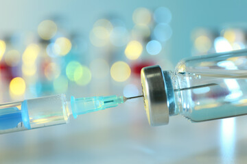 Filling syringe with medication from vial against blurred background, closeup. Vaccination and immunization