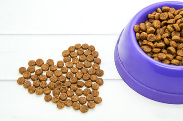 Heart lined with dry animal food and plastic bowl filled with food. Caring for and loving pets. Healthy balanced food for cats and dogs. 