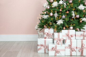 Beautiful decorated Christmas tree and gifts near pink wall. Space for text