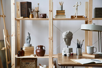 Unique artist workspace interior with stylish desk, wooden easel, bookcase, artworks, painting...