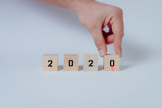Close up of hand completing the year 2020 with symbolic drops of blood on wooden cubes. White background, concept