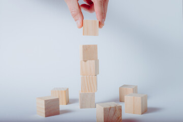 Hand completing tower made of wooden cubes. White background