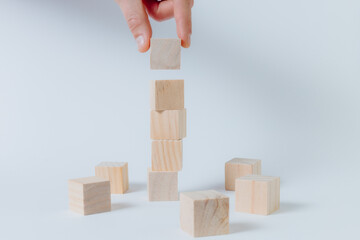 Obraz premium Hand completing tower made of wooden cubes. White background