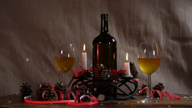 still life on a decorative background with a shot of firecrackers and confetti. candlestick, burning candles, fir cones, streamer, a bottle of wine and glasses.
