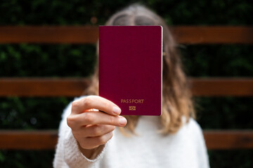 Young woman holding an international passport in front of her face. Travel concept.