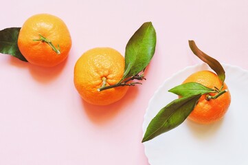 Three juicy sweet tangerines with green leaves on a pink background. Mandarin orange
