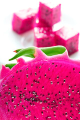 Close-up macro shot of pitaya, pitahaya dragon fluit sliced in half. Exotic superfood vibrant cactus fruit. Magenta pink colored flesh with black seeds. Sliced cubes on white background out of focus.