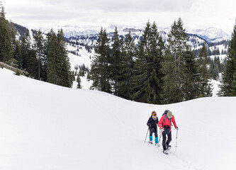 Senior couple is snowshoe hiking in alpine snow winter mountains. Allgau, Bavaria, Germany.