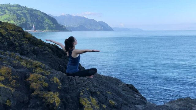 Girl Meditating at the Sea View. Meditation on the Rock. Young Woman Relaxing Alone in a Peaceful Place.
