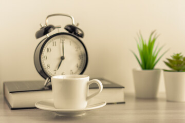 A small Cup of morning coffee, an alarm clock, and a book on the table.