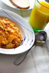Breakfast with a bowl of cornflakes and a glass of orange juice.