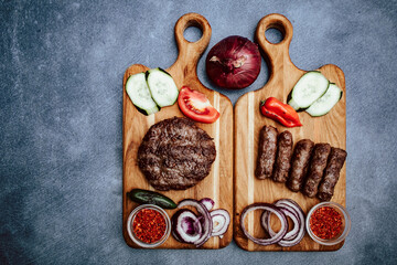 Top view of wooden kitchen board with vegetables and grilled meat.