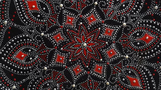 Decorative ceramic plate with red and silver colors, painted plate rotating on background, closeup, top view. Decorative porcelain plate painted with acrylic paints, handwork, dot painting