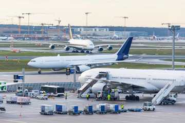 Busy airfield view with airplanes and service vehicles. View of International Airport with planes, gangways, trucks and service equipment. Travel and industry concepts. - obrazy, fototapety, plakaty