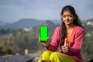 Young indian village girl showing a mobile phone with green screen with thumbs up - Powered by Adobe