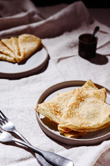 Traditional Russian crepes or pancakes on gray plates over greige linen tablecloth. Pancake week or Shrovetide