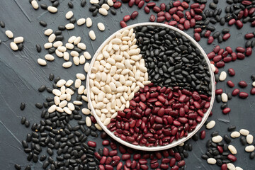 Obraz na płótnie Canvas beans in white ceramic plate. bowl of beans. black bean, red kidney bean and white bean. navy bean, cannellini bean, white kidney bean on dark gray background and scattered various beans