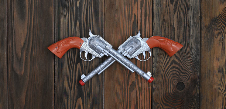 two cowboy toy revolvers on a wooden wall