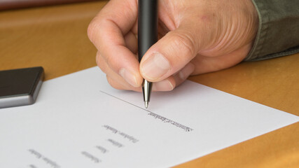 A hand holding a pen. A hand of a man signing a document. Agreement. accordance.
