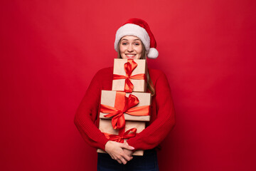Excited surprised woman in red santa claus outfit holding stack presents isolated on the red background